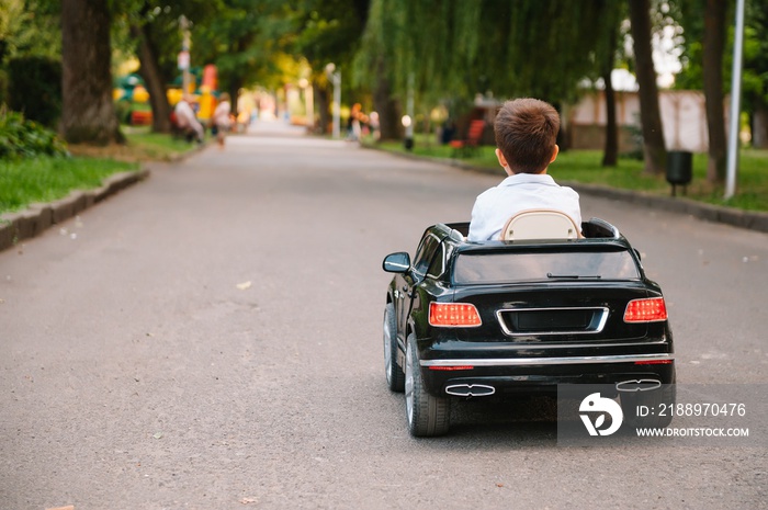 Cute boy in riding a black electric car in the park. Funny boy rides on a toy electric car. Copy spa