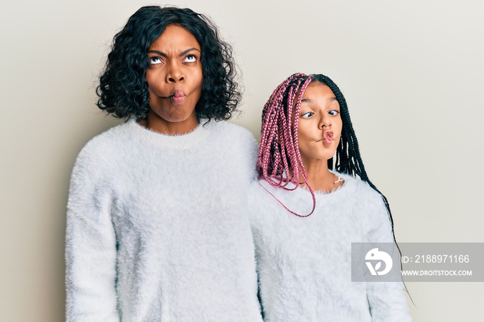 Beautiful african american mother and daughter wearing casual winter sweater making fish face with l