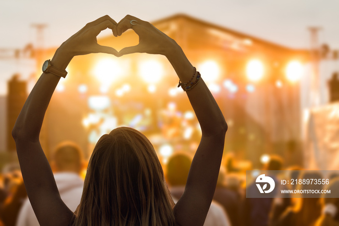 Girl with heart-shape symbol enjoying her favorite group on the concert.