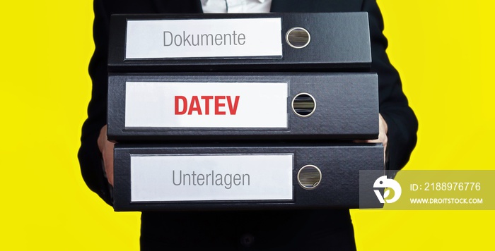 DATEV – Finanzen/Wirtschaft. Mann trägt einen Stapel Aktenordner. Ein Ordner hat die Beschriftung DA