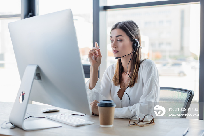 businesswoman in headset looking at computer monitor while pointing with finger.