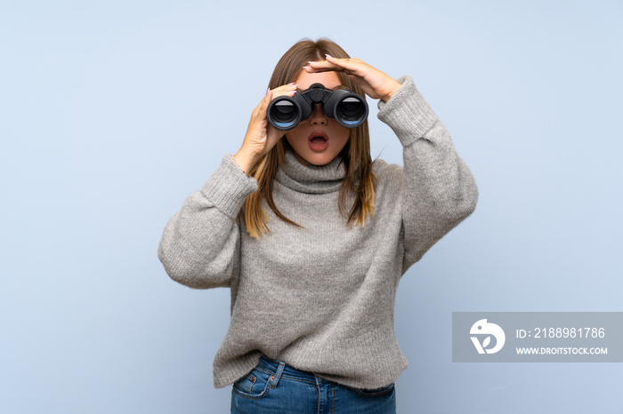 Teenager girl with sweater over isolated blue background with black binoculars