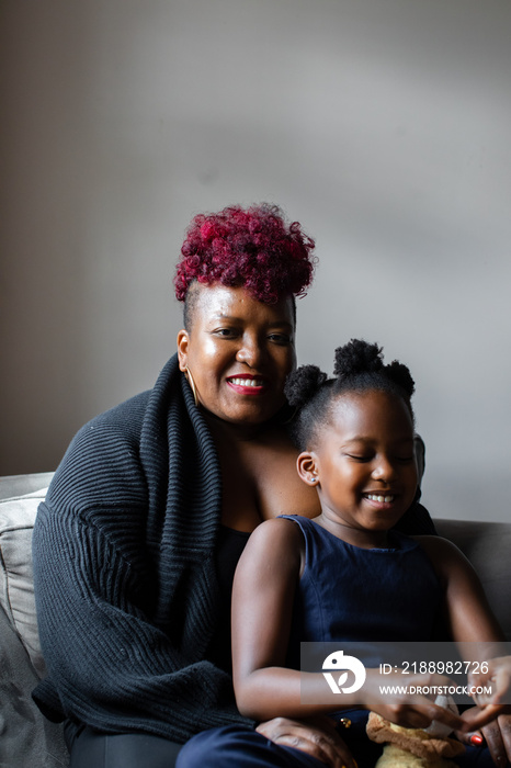 African American mother and daughter sitting on couch smiling together