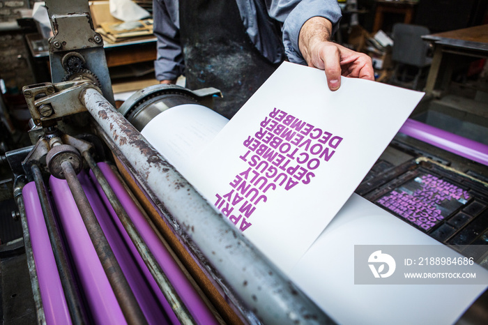 Midsection of craftsman taking printed paper out of roller in workshop