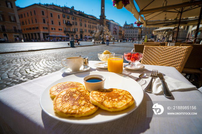 Italian breakfast including pancakes fruits and drinks on the background of Piazza Navona in Rome,It