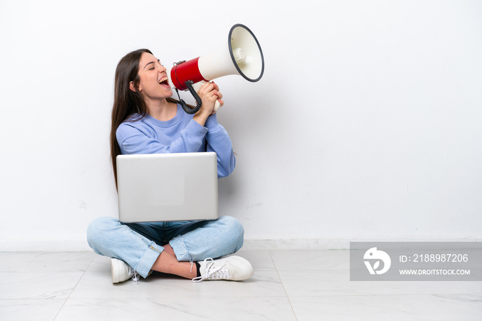 Young caucasian woman with laptop sitting on the floor isolated on white background shouting through