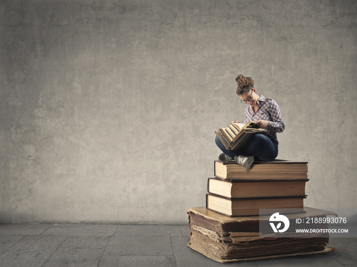 Young woman reading while sitting on a pile of books