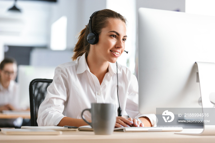 办公室呼叫中心里快乐快乐的商务女性戴着耳机用电脑工作。