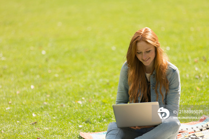 Smiling young woman with laptop in sunny park grass