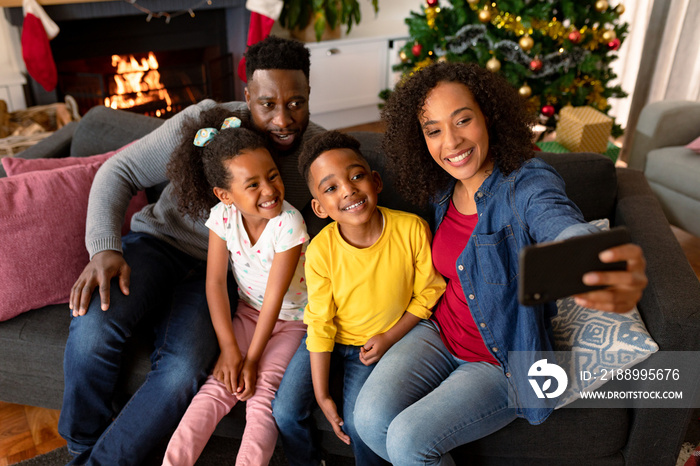 Happy african american family sitting on sofa and taking selfie, christmas decorations in background