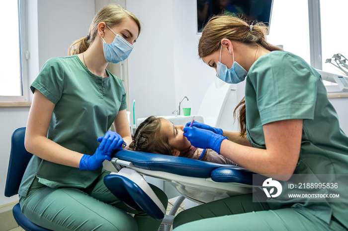 Qualified dentists treat teeth on a small childs dental chair.