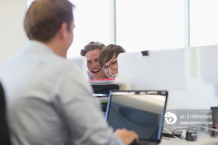 Playful business people watching colleague at laptop