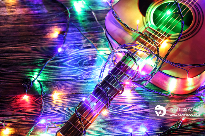 Acoustic guitar with Christmas lights on wooden background