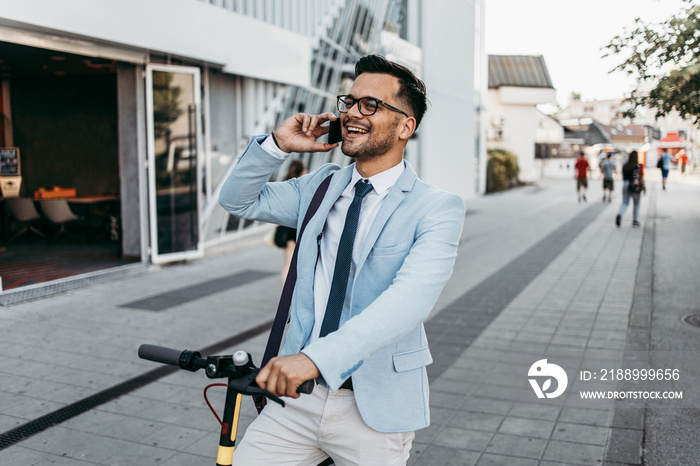 Young modern man using smart phone and driving electric scooter on city street. Modern and ecologica