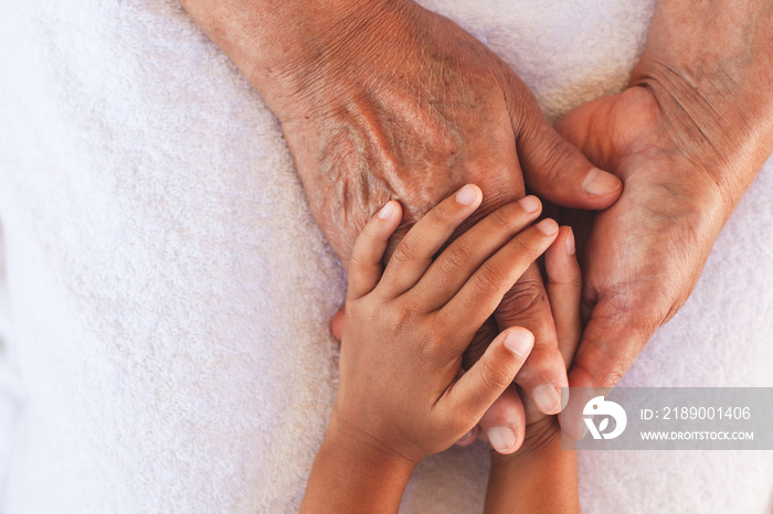 Hands of asian child girl holding elderly grandparent hands wrinkled skin with feeling care and love