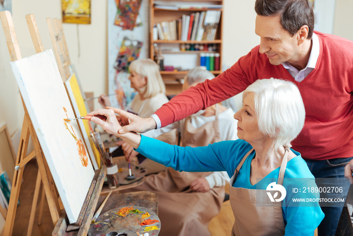 Delighted artist helping elderly woman in painting studio