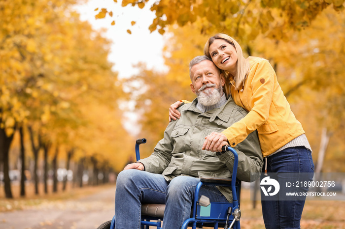 Woman with her elderly father in wheelchair outdoors on autumn day