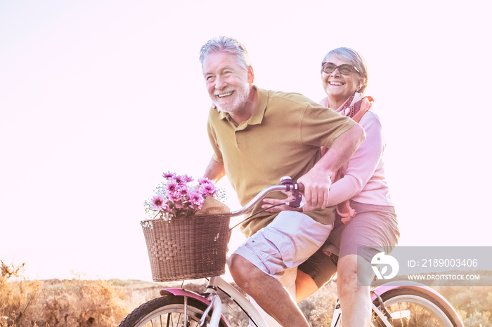 Cheerful mature couple of senior enjoy the outdoor leisure activity together riding a bike and laugh