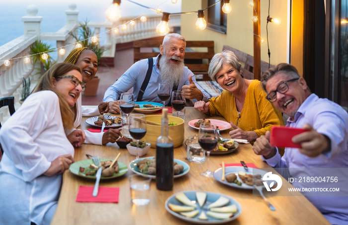 快乐的多种族资深朋友在一起用餐，同时用手机智能手机自拍