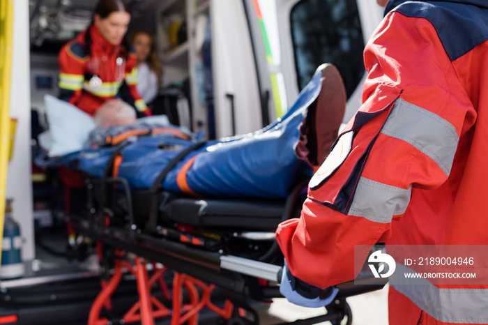 Selective focus of paramedic in uniform carrying stretcher with patient in ambulance ca outdoors