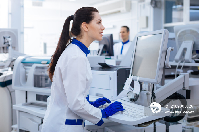 Nice touch. Energetic positive female laboratory assistant looking at the screen, typing while stand