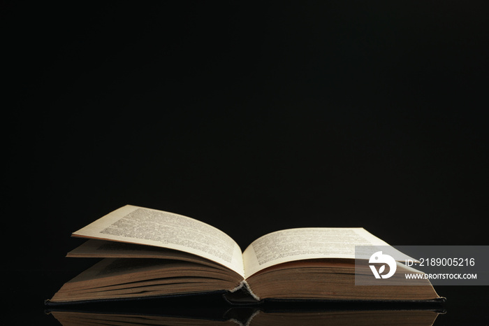 One open old book on a glass table. Beautiful dark background....