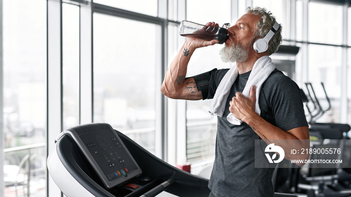 Mature man drinking water from bottle, the towel on shoulder