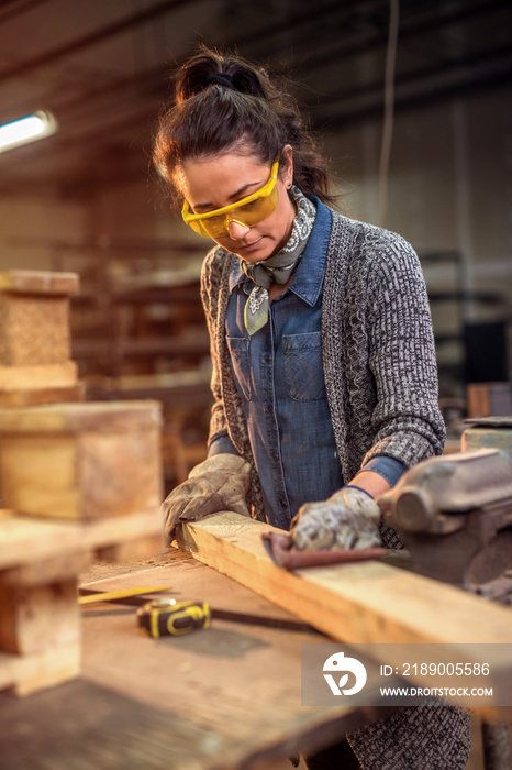 Middle aged professional female carpenter working with sandpaper in her workshop.