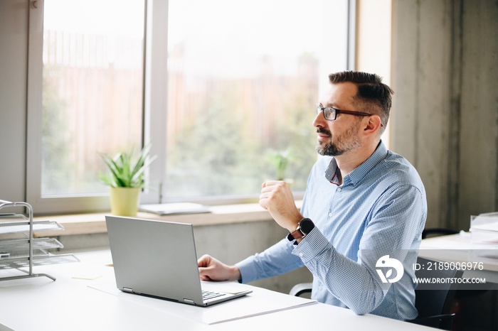 Middle aged handsome man in shirt working on laptop computer in office