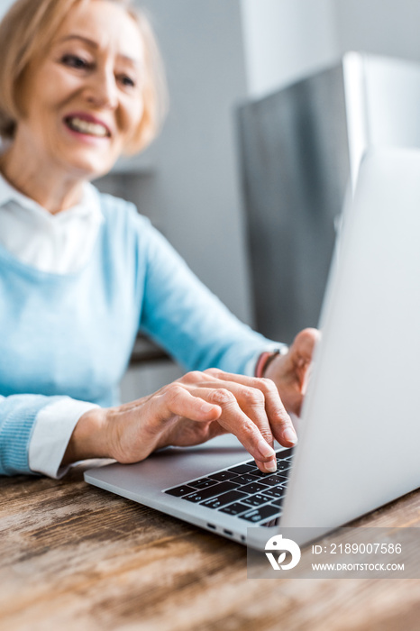 selective focus of smiling senior woman typing on laptop at home