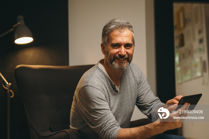 portrait of bearded middle aged man using cellphone relaxed in sofa at his home