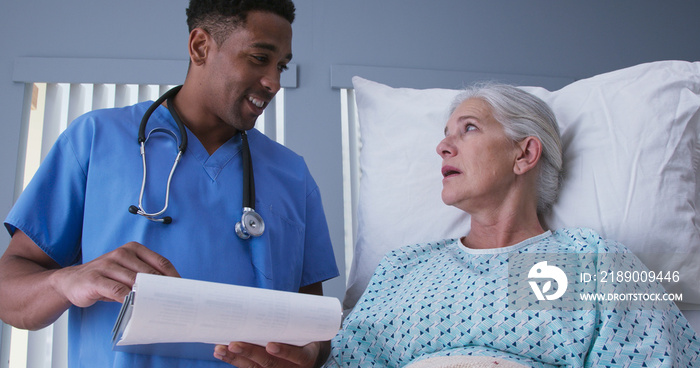 Millennial male nurse reading doctors notes to elderly female patient. Ill senior woman resting in h