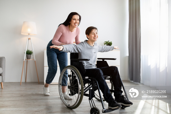 Full length of young mom and her impaired son in wheelchair having fun together at home