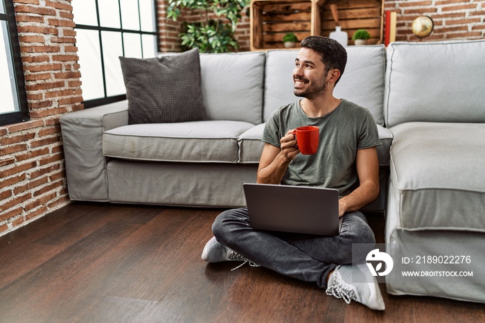 Young hispanic man using laptop and drinking coffee at home