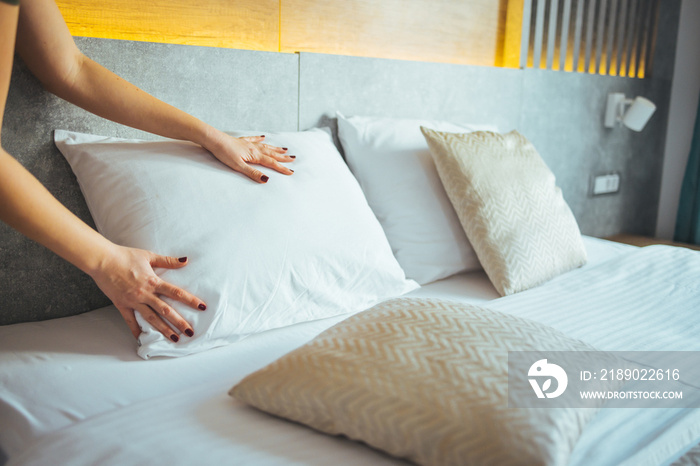 Maid making bed in hotel room. Female hands corrected pillow on the bed. Concept on preparation of b