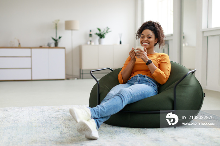 Calm black woman having rest at home drinking coffee