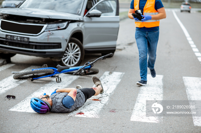 Road accident with injured cyclist lying on the pedestrian crossing near the broken bicycle and car 