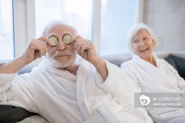 Senior couple in white robes enjoying spa procedures and having fun