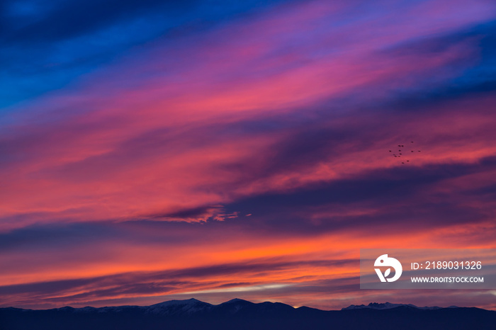 日落/日出，鲜艳的品红色天空，云朵和山脉的深色轮廓。