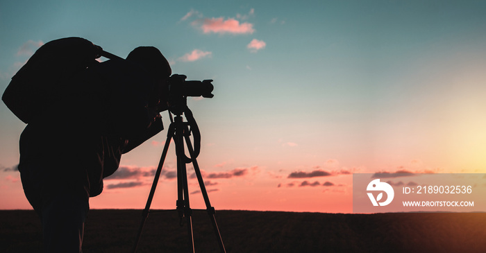 photographer with a tripod and camera takes a landscape during sunset in a large open area