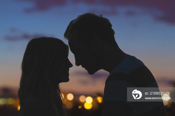 一对年轻情侣接吻的剪影，背景是城市全景。