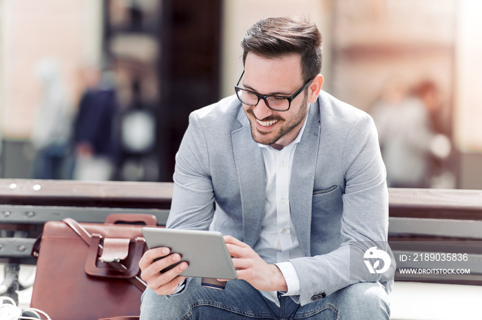 Young businessman using a tablet on a bench in the city