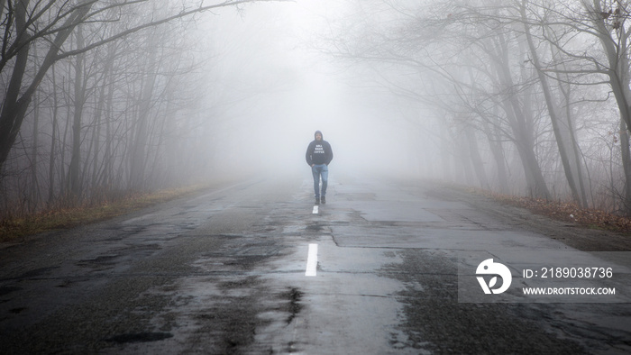 孤独的男人走在远离雾霾的路上。晨雾中的乡村景观。温暖的秋色。