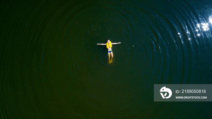 Small boy in yellow life vest bathes on his bach in the river. Kid swims in life-saving jacket in a 