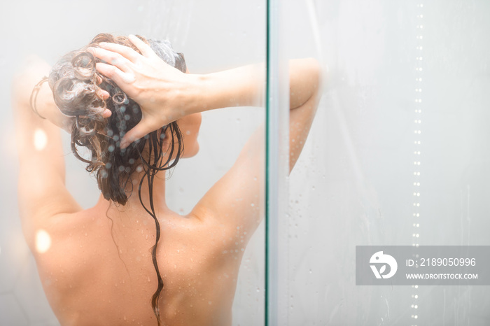 年轻女子在淋浴时用洗发水洗头。后视图