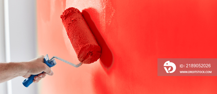 Male hand painting wall with paint roller. Painting apartment, renovating with red color paint