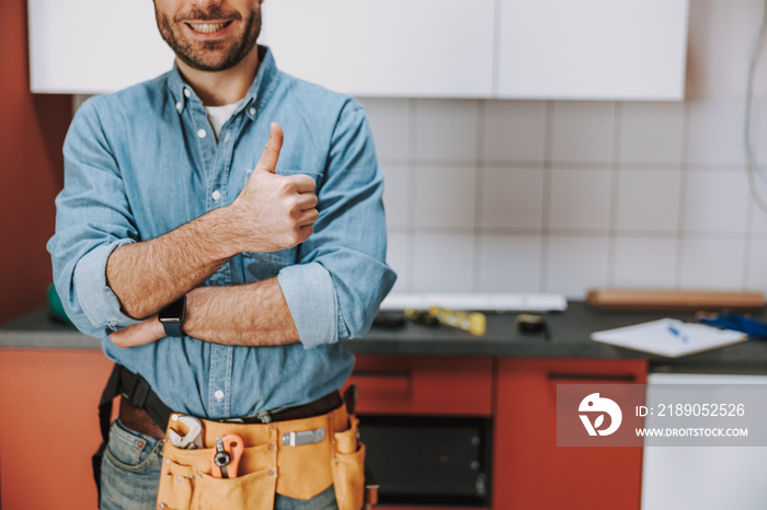 Smiling repairman staying with tool belt at home