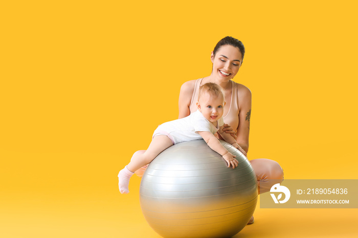 Young sporty mother and her baby doing exercises with fitball on color background