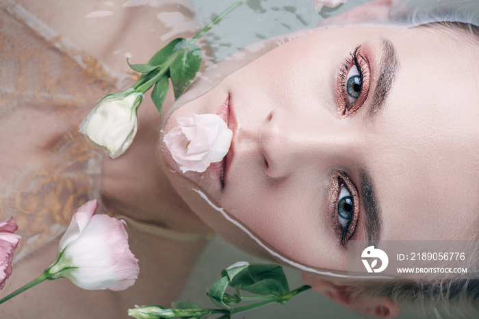 top view of beautiful woman lying in clear water with flower in mouth