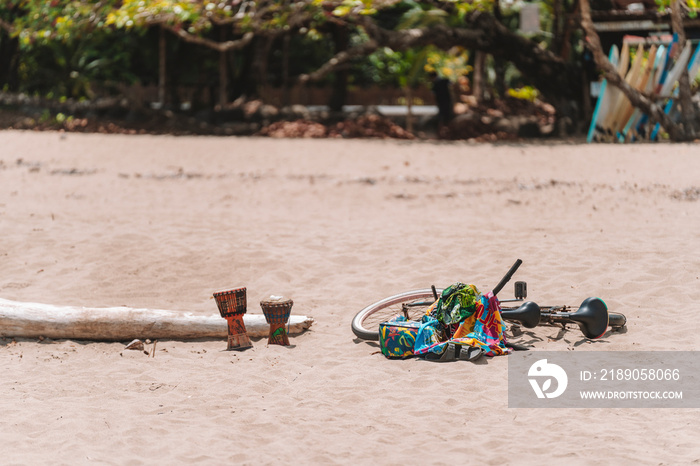 Imagen de tambores y una bicicleta con mantas coloridas sobre la arena de la playa en un día soleado